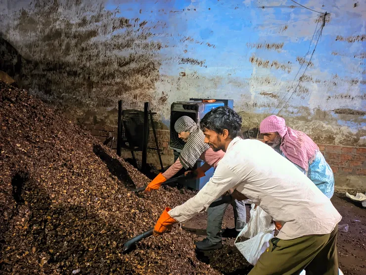 Team of workers processing cashew shell material by hand